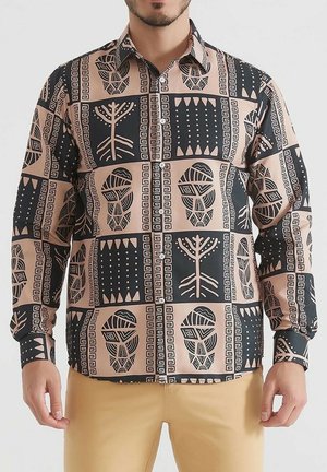 Chemise à manches longues avec un motif géométrique beige et noir, présentant des motifs tribaux, et un col classique. Tissu au toucher lisse.