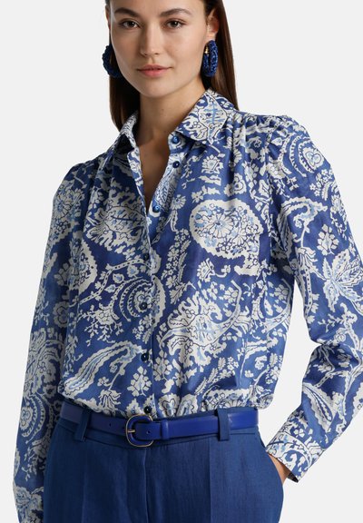 Blauwe en witte gestreepte blouse met een kraag, knopen en gathered mouwen, gecombineerd met een blauwe riem en hoge taillebroeken.
