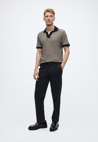 Īsām piedurknēm polo krekls gaiši brūnā dzijā ar melnām apkakles un aproču detaļām, kombinēts ar melnām piesaistītām biksēm un melniem apaviem. Vienkāršs dizains.