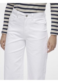 Jeans de mezclilla blanca con un corte relajado, que presentan un diseño clásico de cinco bolsillos, presillas para cinturón y un cierre de botón metálico. Textura suave.