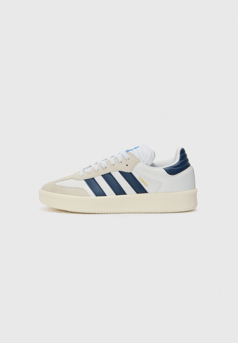 Vita och marinblå sneakers med mocka och lädermaterial, med tre marinblå ränder, vita snören, en strukturerad krämfärgad sula och blå detaljer.
