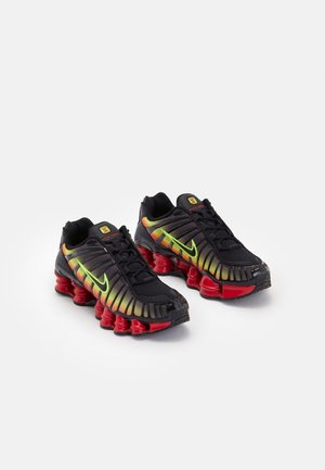 Chaussures de sport noires avec un swoosh Nike jaune-vert néon et des accents orange en dégradé, dotées de semelles ressorts rouges caractéristiques absorbant les chocs.