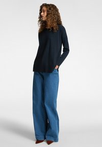 Maglione lavorato a maglia blu navy con scollo rotondo, abbinato a jeans in denim a vita alta e gamba ampia, e tacchi a punta marroni. Tessuto liscio, vestibilità rilassata.