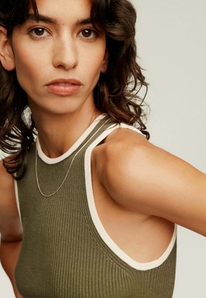Top de tirantes de canalé en verde oliva con ribetes blancos, que presenta un diseño ajustado y amplias sisas. Un collar de cadena plateada añade un detalle sutil.