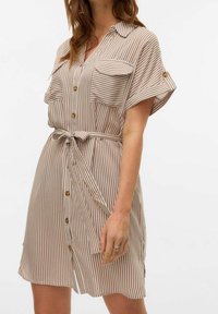 Abito a righe a maniche corte in beige e marrone, con chiusura a bottoni frontale, due tasche sul petto, vita con cintura e tessuto morbido.