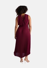 Robe plissée bordeaux avec une taille cintrée, un dos ouvert et des fines bretelles. Longueur jusqu'au sol avec une texture de tissu lisse et fluide.