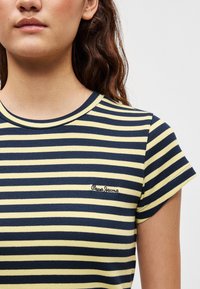 Ριγέ μπλούζα σε μπλε ναυτικό και κίτρινο χρώμα, με κοντά μανίκια, στρογγυλή λαιμόκοψη, υφή ριπ, με κεντημένο το λογότυπο "Pepe Jeans" στο αριστερό στήθος.