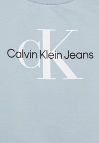 T-shirt di cotone azzurro chiaro con scollatura rotonda, caratterizzata da un testo nero audace "Calvin Klein Jeans" e un grande logo stilizzato "CK" in bianco.