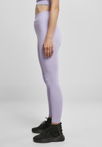Lyse lilla leggings laget av elastisk stoff, med høy midje og glat overflate, akkompagnert av svarte høye sneakers.