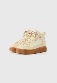 Kremfarvede high-top sneakers med mønstrede snørebånd og tykke brune gummisåler på en hvid baggrund.