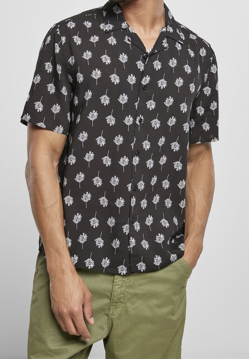 Chemise noire à manches courtes avec un motif de feuilles blanches, confectionnée en tissu léger, coupe décontractée et col à boutons.