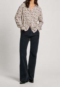 Långärmad skjorta med knappar i krämfärgad med blommönster i rött, blått och grönt. Matchad med mörka vida byxor och svarta stövlar.