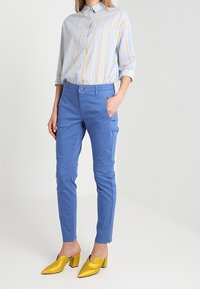 Světle modrá pruhovaná košile se žlutými detaily, modré úzké kalhoty a žluté mule na blokovém podpatku. Hladká tkanina a pohodlný design.