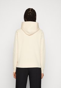 Sudadera con capucha de color crema y corte relajado, que cuenta con un bolsillo tipo canguro y puños de canalé. Textura suave, diseño minimalista.