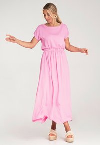 Różowa maxi sukienka z krótkimi rękawami i elastycznym pasem. Lekka tkanina, zwiewny krój, w połączeniu z beżowymi sandałami na koturnie.