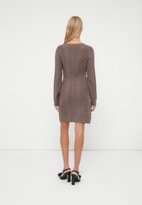 Rochie tricotată maro, cu mâneci lungi, talie ajustată, lungime deasupra genunchiului și mansete cu model din caneluri. Purtați cu sandale negre cu toc.