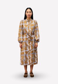 Braun und weiß gemustertes Hemdblusenkleid mit langen Ärmeln, einem Kragen und einem Gürtel in der Taille. Der Stoff wirkt leicht und hat eine glatte Textur.