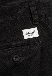 Black corduroy pants featuring a textured surface, a rear pocket with a white label, and a round black button for closure.