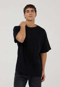 T-shirt nera oversize in cotone con collo rotondo e maniche corte. Caratterizzato da una vestibilità rilassata e una texture liscia, design minimalista.