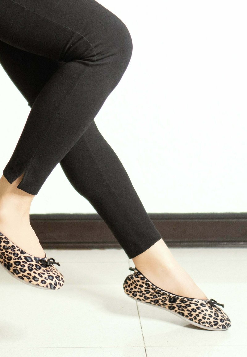 Ballerines en imprimé léopard avec des accents noirs, bout arrondi, semelle plate et un petit noeud décoratif. Associées à des leggings noirs.