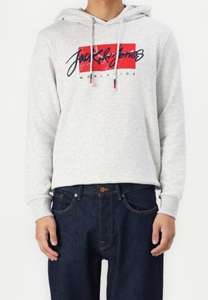 Grijze hoodie gemaakt van een katoenmix, met een rood en blauw logo ontwerp op de voorkant. Gepaarde met donkerblauwe jeans, die een ontspannen pasvorm hebben.