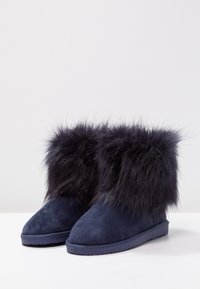 Botines de ante azul marino con un puño de piel sintética, que presentan una punta redonda y una suela de goma, destacando la textura y la calidez.