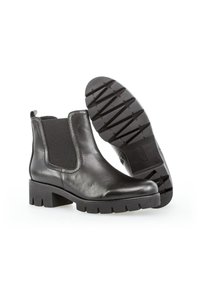 Botas Chelsea de cuero negro con paneles laterales elásticos, suela de goma gruesa y patrón de agarre texturizado en la suela. Diseño de punta redondeada.