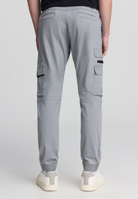 Jasnoszare spodnie cargo z elastycznymi ściągaczami, bocznymi kieszeniami i kontrastującymi czarnymi akcentami na kieszeniach. Wykonane z gładkiego materiału.