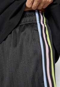 Črne hlače z navpičnimi teksturiranimi črtami in večbarvnimi bočnimi zadrgami v modri, roza in zeleni barvi. Prijeten kroj z elastičnim pasom.