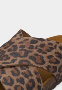 Κοντινό πλάνο καφέ σανδαλιού χωρίς κορδόνια με μαύρο και σκούρο καφέ λεοπάρ σχέδιο και φαρδιές χιαστί λουριά.