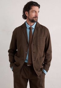 Brun bomuldsblazer med notched krave, frontlomme, parret med en lyseblå skjorte og en struktureret brun slips.