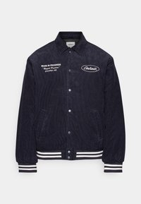 Marineblaue Cordjacke aus Cord mit Druckknöpfen, gestreiften Bündchen und Saum, Vorderentaschen und weißen, gestickten Carhartt-Logos auf der Brust.