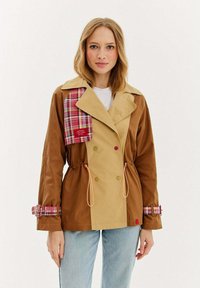 Dvojradový, dvojtónový kabát v hnedom a khaki so škótskymi akcentmi. Obsahuje sťahovaciu pásku v páse a škótske manžety. Hladká textúra.