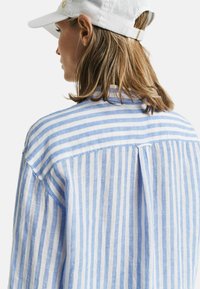Camicia in lino leggera e traspirante con righe verticali blu e bianche. Presenta una piega sul retro e una vestibilità rilassata. Design del colletto semplice.