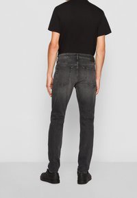 Tmavě šedé džíny se slim fit, s zadními kapsami, černým pasem a hladkým denimovým povrchem. Stylizované s černým tričkem.
