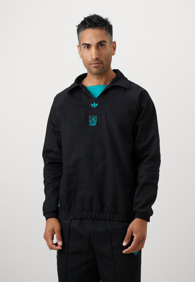 Sort pullover med en afslappet pasform, der har krave og elastisk talje. Smykket med turkis Adidas-logo og Liverpool-våbenskjold.