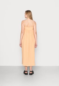 Vestido maxi cor pêssego com corpete ajustado e saia solta, franzida. Apresenta alças finas e um tecido leve e texturizado.