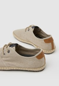 Beige Leinenschuhe mit runden Zehen, Jute-Seilsohlen und braunen Lederakzenten an den Fersen. Mit schnürähnlichen Bändern verschnürt.
