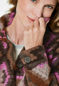 Manteau en laine présentant un mélange de motifs marron et rose, un col cranté et des boutons foncés, avec une finition douce et texturée.