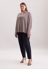 Blusa a maniche lunghe, con motivo in colori chiari, dotata di scollatura a V e vestibilità rilassata, abbinata a pantaloni navy e sandali neri.