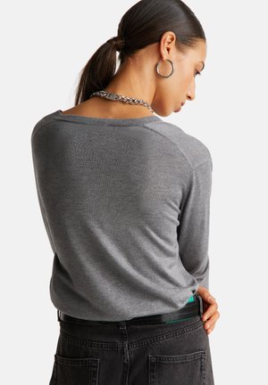 Maglione grigio a maniche lunghe con una vestibilità leggermente ampia e colletto a coste, abbinato a jeans neri a vita alta e una collana a catena.