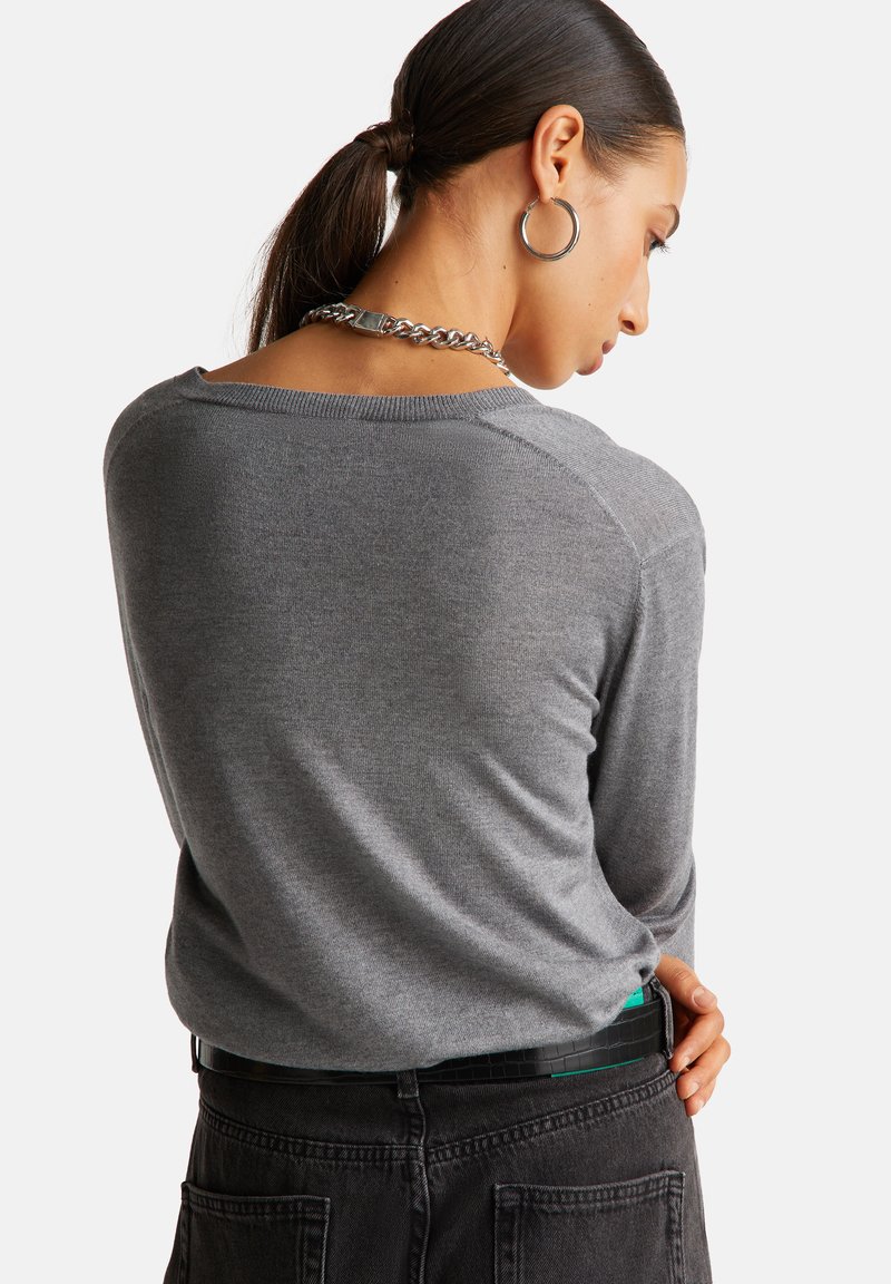 Grauer, langärmeliger Pullover mit legerem Schnitt und geripptem Halsausschnitt, kombiniert mit hoch taillierten schwarzen Jeans und einer Kettenhalskette.
