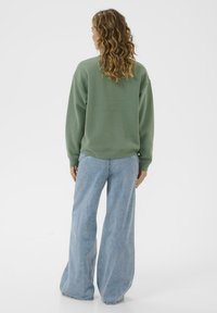 Sweatshirt vert oversized avec un col rond, assorti à un pantalon en jean bleu clair à jambes larges. Texture lisse, coupe décontractée et épaules tombantes.