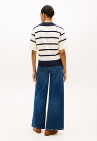 Πλεκτό μπλουζάκι με κοντά μανίκια σε ναυτικό μπλε και άσπρες ρίγες με γιακά, συνδυασμένο με ευρύχωρο παντελόνι τζιν σκούρου μπλε και καφέ παπούτσια.