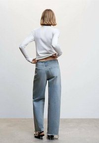 Biała koszula z długim rękawem w połączeniu z jasnoniebieskimi, luźnymi dżinsami z postrzępionym dołem i tylnymi kieszeniami. Czarne szpilki dopełniają całość.