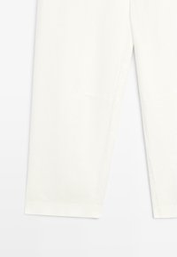 White tailored pants with straight legs and visible stitching detail near the knees and hems, displayed on a flat surface.