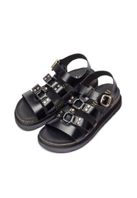 Sandalias de cuero negro con múltiples detalles de tiras, tachuelas metálicas y una correa con hebilla en el tobillo, además de una suela acolchada.
