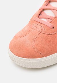 Rosa mockasneaker med matchande snören, har en vit gummisula med textur och sydda detaljer på ovansidan.