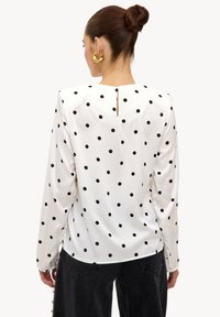 Blouse à manches longues en satin blanc à pois noirs, avec un col rond et un petit détail œillet au dos.