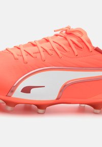 Bright coral soccer cleat featuring a smooth synthetic upper, white mesh panel, pink accents, and molded studs for traction.